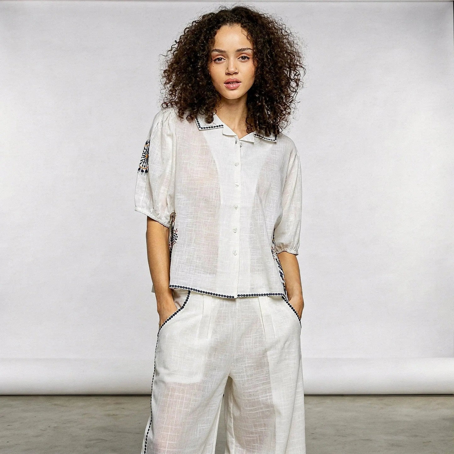 View of a relaxed fit short sleeve button down shirt featuring floral embroidery in soft pastel colors on a light background
