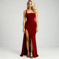 View of a fitted square neck maxi evening dress in deep burgundy, featuring a high slit and flowing fabric